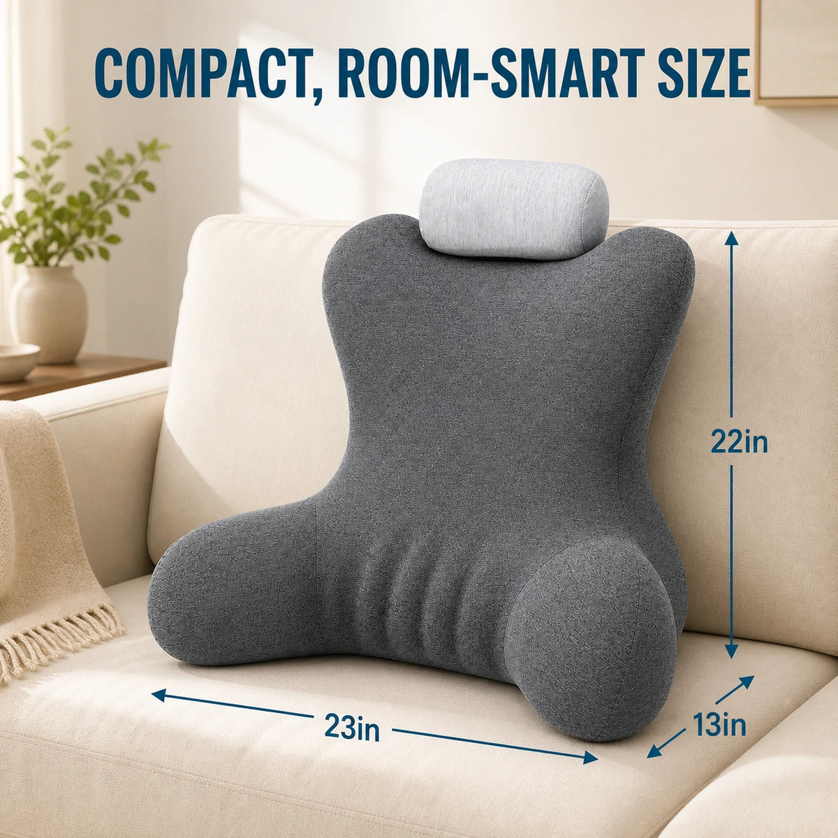A dark gray contoured lumbar pillow with a matching light gray headrest cushion, displayed on a beige sofa. Blue dimension lines and text overlay indicate its size as 23 inches wide, 22 inches tall, and 13 inches deep, with the headline 'COMPACT, ROOM-SMART SIZE' at the top.