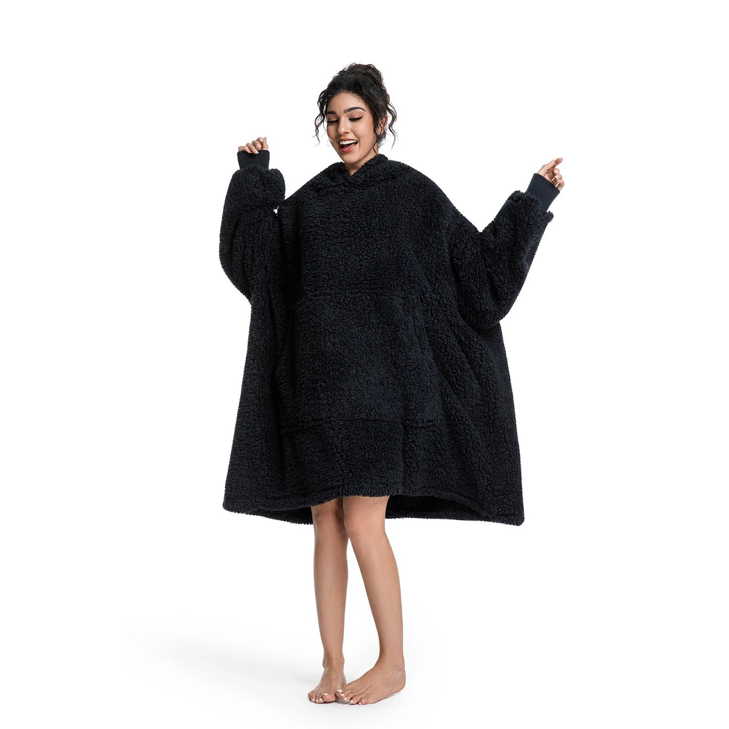 A woman modeling a black sherpa fleece hooded robe or poncho with wide sleeves, standing barefoot against a plain white background.