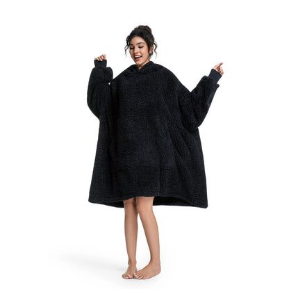 A woman modeling a black sherpa fleece hooded robe or poncho with wide sleeves, standing barefoot against a plain white background.